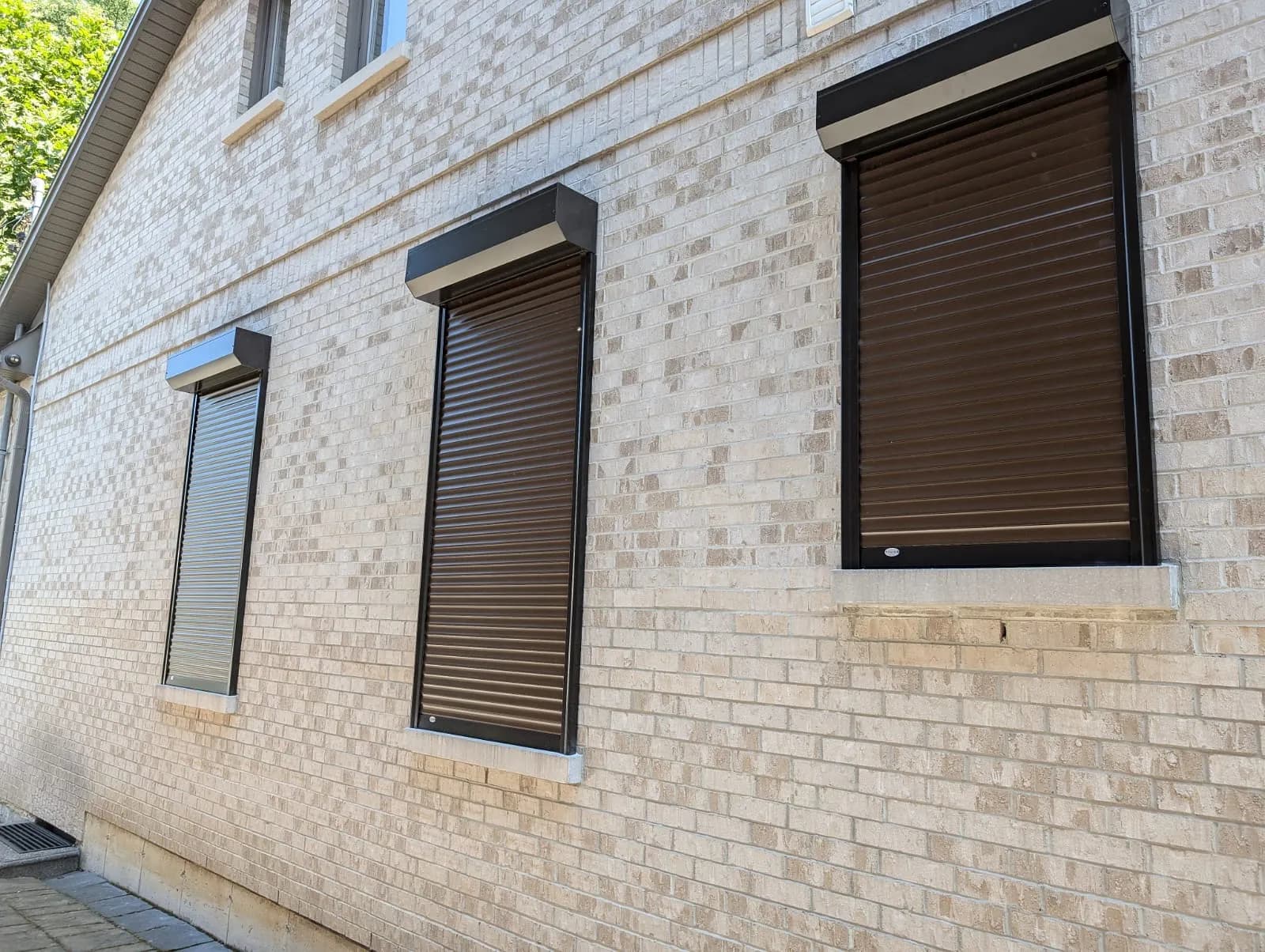 Three black-framed aluminum roll shutters deployed across a brick Ontario exterior