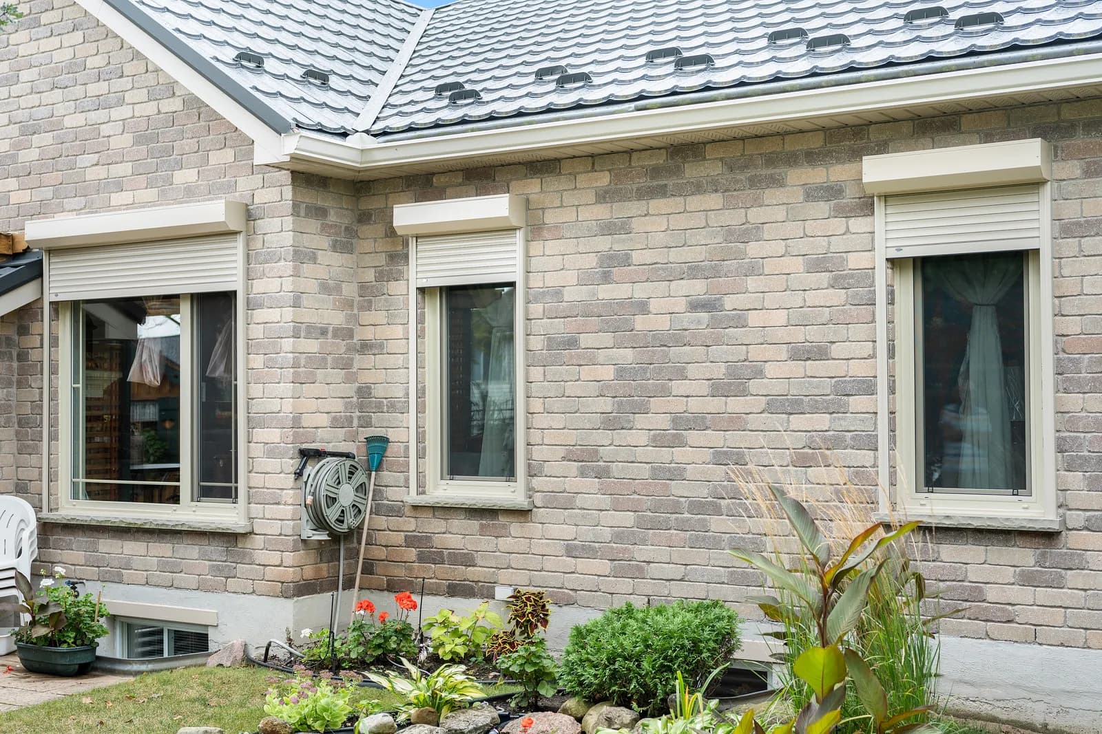 Brick bungalow with cream aluminum roll shutters retracted above the windows