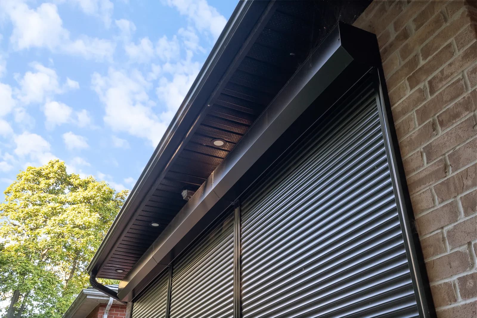 Black aluminum roll shutter deployed under a brown soffit with storm-front sky