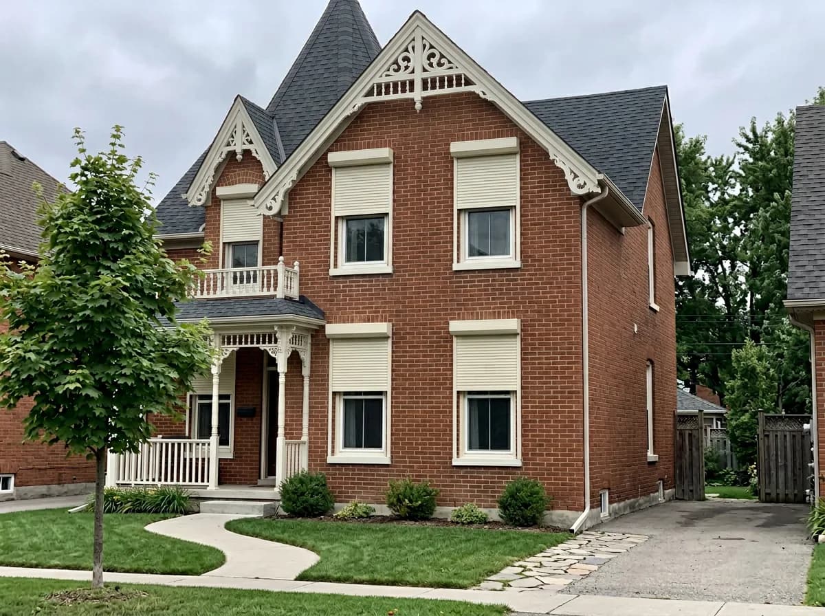 Cream aluminum roll shutters deployed across the front windows of a red-brick Victorian Ontario home for security and storm protection