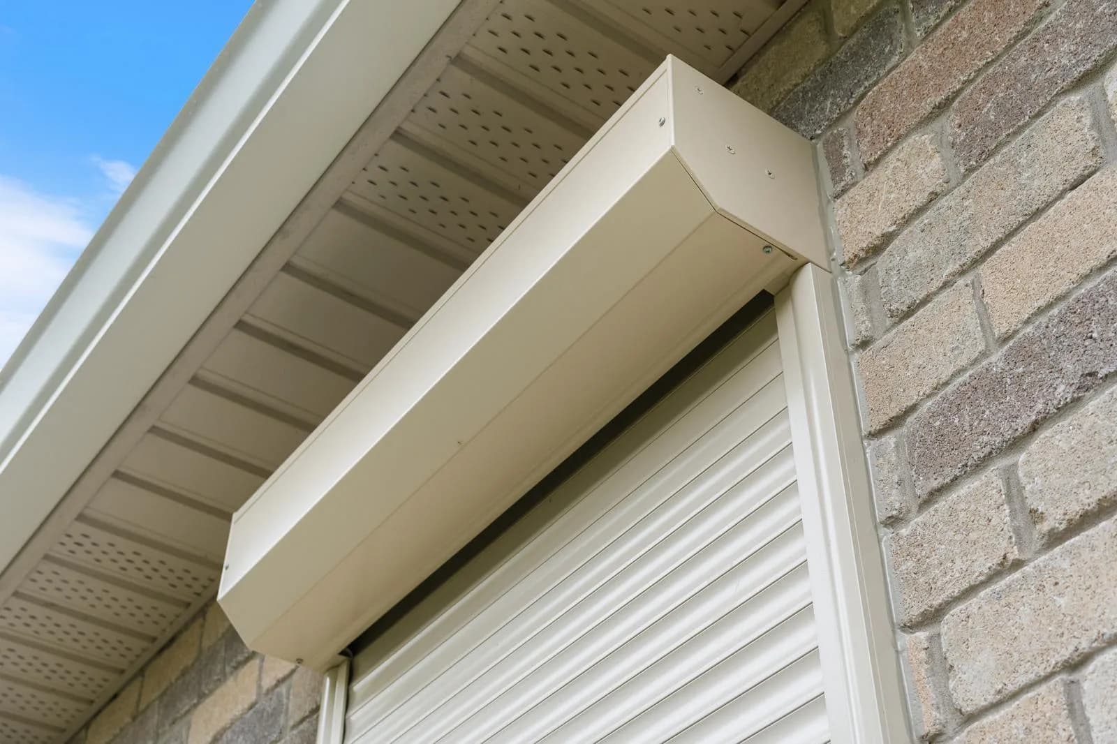 Close-up detail of a cream aluminum roll shutter headbox tucked under the soffit on a brick exterior