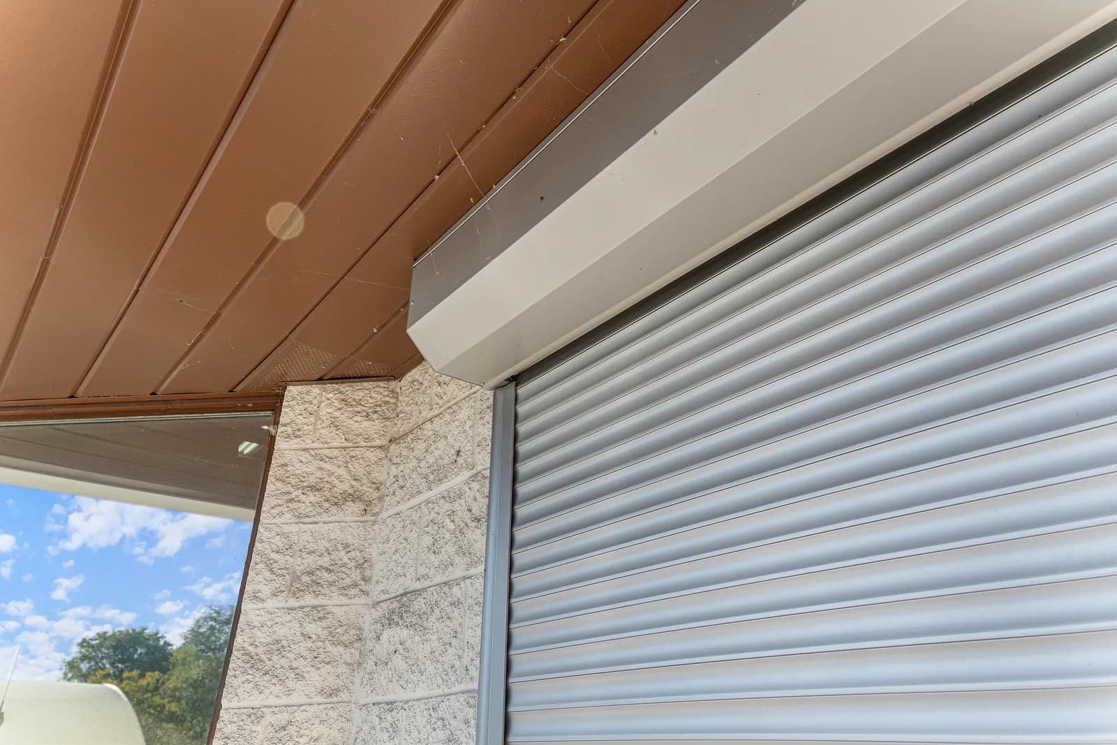 Close-up of light-grey aluminum roll shutter slats with the headbox mounted to a wood-clad ceiling