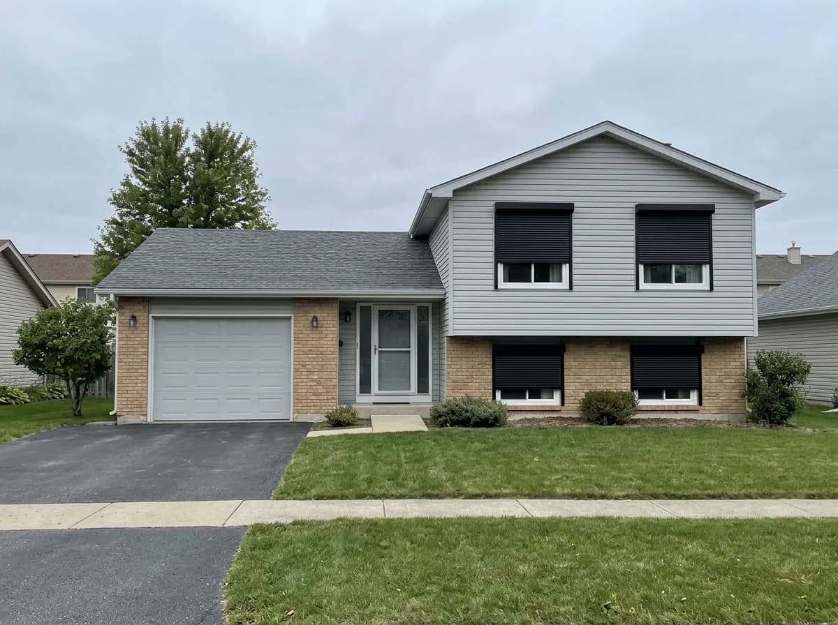 Grey vinyl split-level Ontario home with black aluminum roll shutters deployed across the front windows