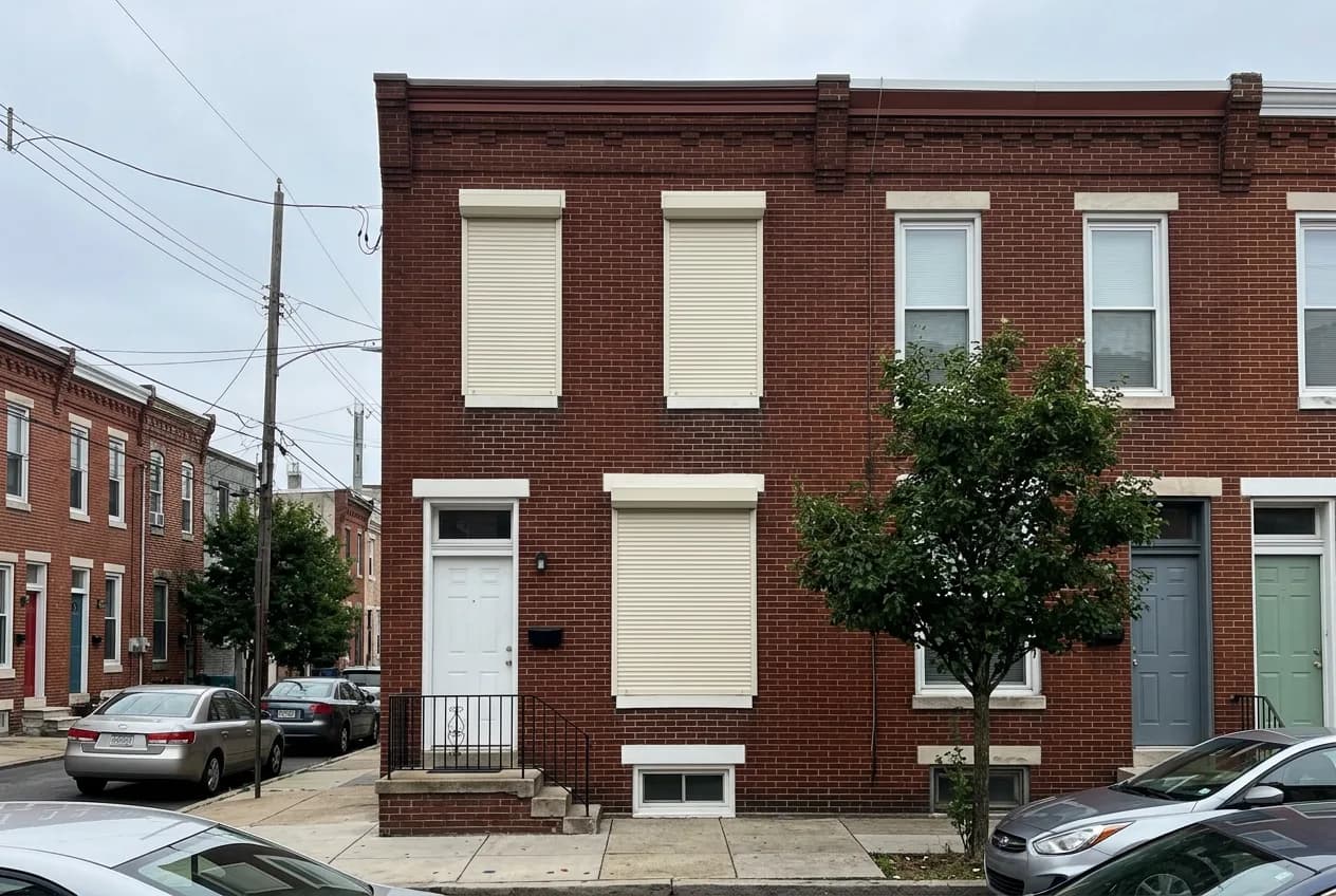 Red-brick urban Ontario row house with cream aluminum roll shutters deployed over the front windows