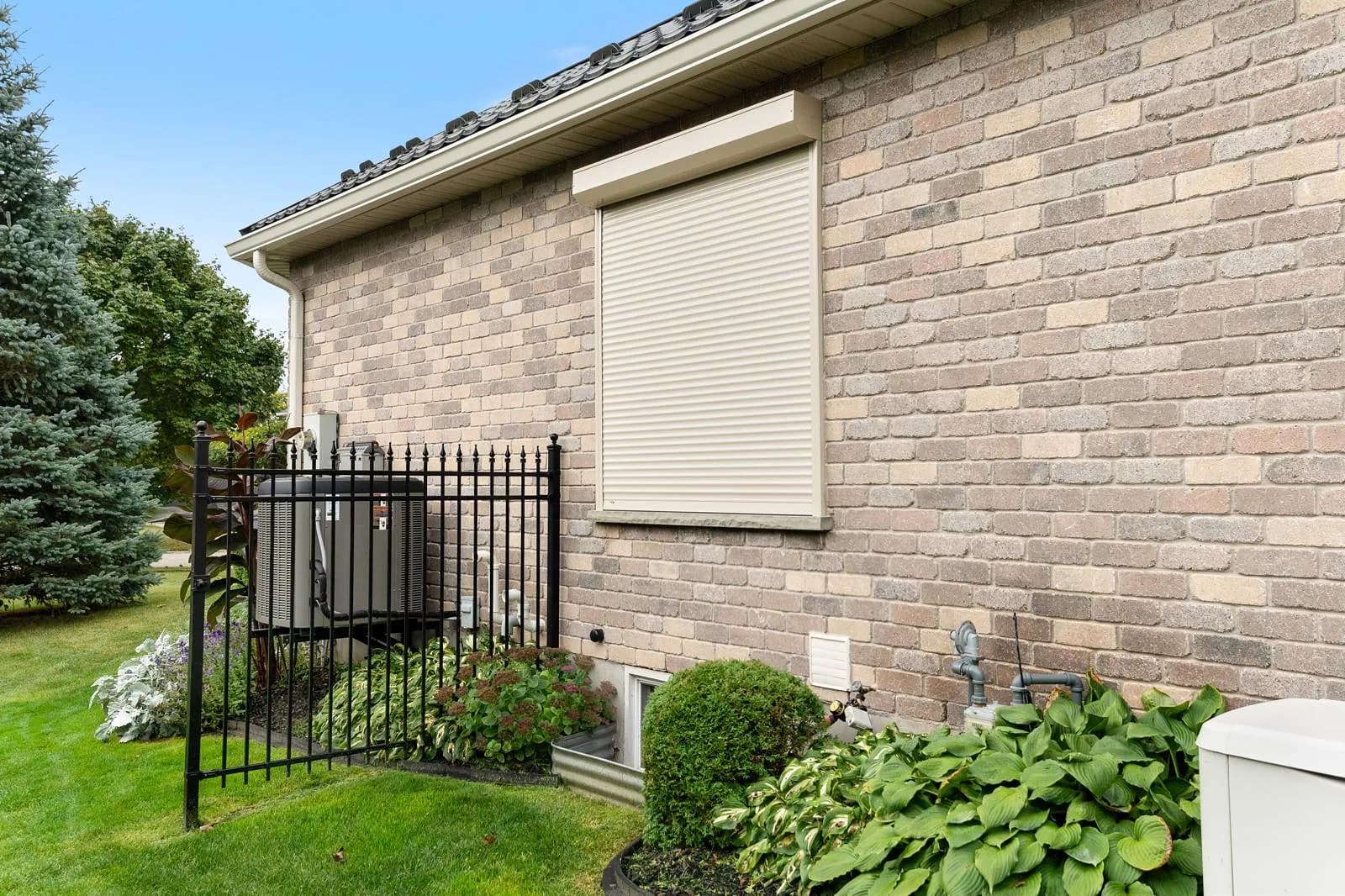 Single cream aluminum roll shutter deployed over a window on a brick exterior wall