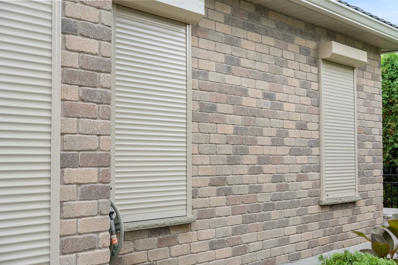 Two cream aluminum roll shutters deployed over windows on a multi-tone brick exterior