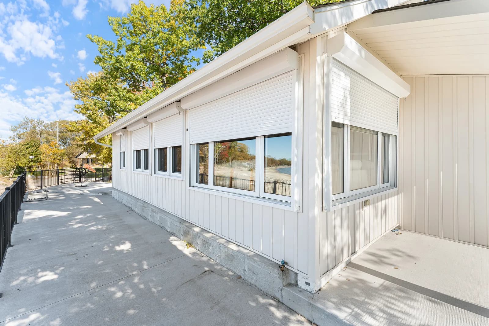 White-clad lake home with cream aluminum roll shutters retracted above the windows