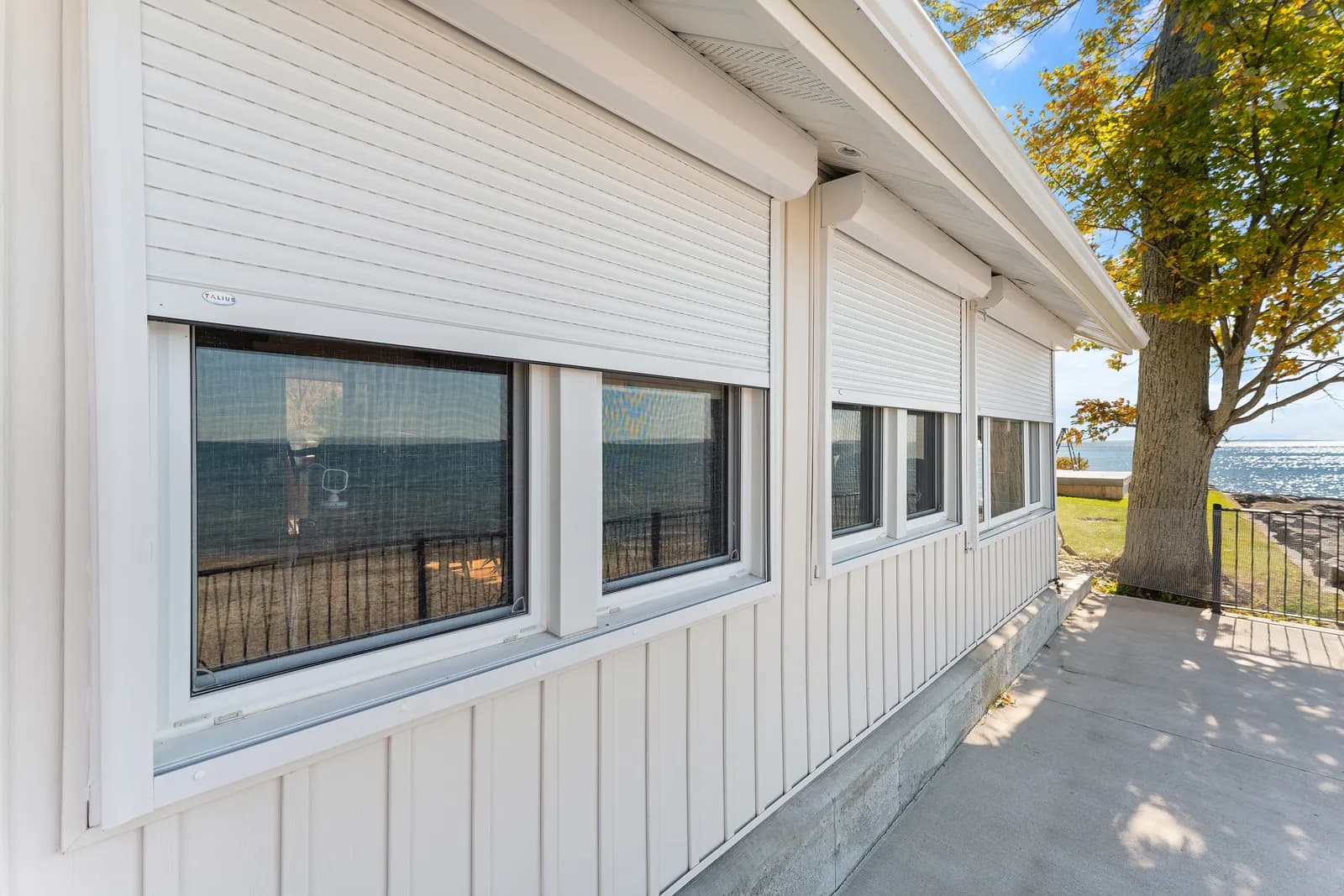 White lake home front windows with cream aluminum roll shutters retracted into headboxes above each opening
